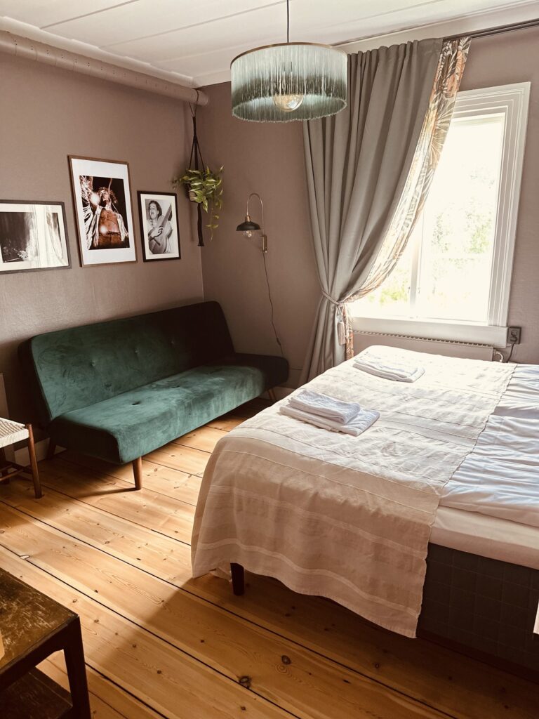 Rum med dubbelsäng, grön soffa och fotografier på väggen